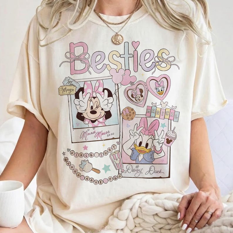 Peut inclure: T-shirt cr&egrave;me avec le mot "Besties" en couleurs pastel. Le t-shirt pr&eacute;sente Minnie Mouse et Daisy Duck dans des cadres de style polaroid, ainsi que d'autres graphiques et du texte. Le design comprend des c&oelig;urs, des &eacute;toiles et les mots "Magical" et "Girls Just Wanna Have Fun".
