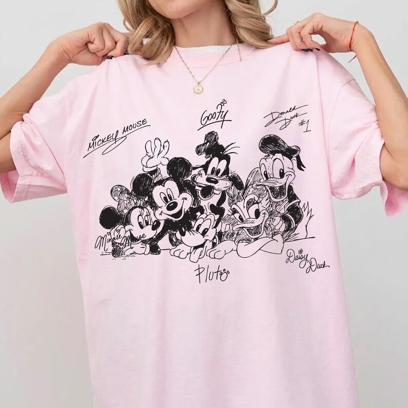 Pu&ograve; includere: T-shirt rosa chiaro con un disegno in bianco e nero di Topolino, Minnie, Pippo, Paperino, Paperina e Pluto. I nomi dei personaggi sono scritti sulla maglietta.