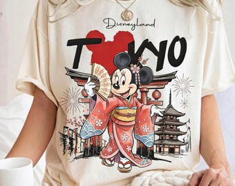 May include: Cream-colored t-shirt featuring a graphic of Minnie Mouse in a kimono, holding a fan. The design includes the text "Disneyland Tokyo" with a red Mickey Mouse head silhouette and Japanese architectural elements.