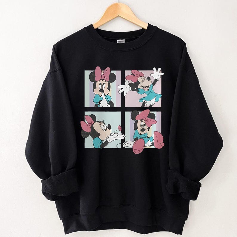 May include: Black sweatshirt featuring a four-panel graphic of Minnie Mouse in various poses. Minnie is depicted wearing a blue dress and a pink bow. The background of each panel is a different pastel color.