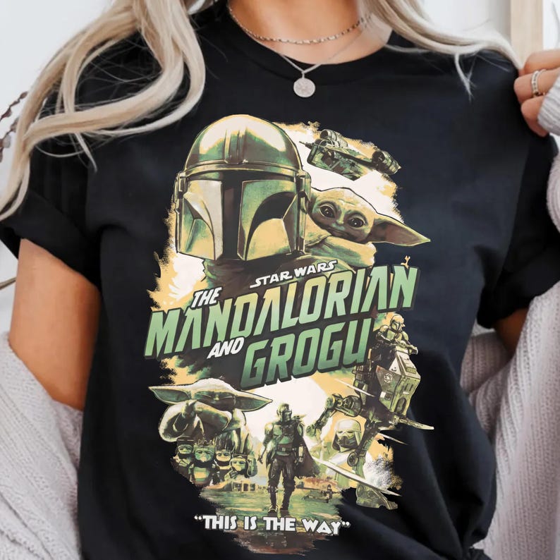 May include: Black t-shirt featuring a Star Wars design with The Mandalorian and Grogu. The graphic includes images of the Mandalorian, Grogu, and various vehicles and characters from the series. Text on the shirt reads "The Mandalorian and Grogu" and "This is the Way."