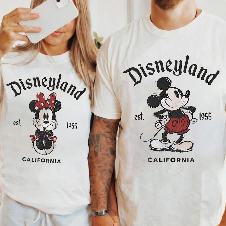 May include: Off-white t-shirts with the Disneyland logo and vintage Mickey and Minnie Mouse graphics. The shirts display "est. 1955" and "CALIFORNIA". One shirt features Minnie Mouse with a red bow, and the other features Mickey Mouse.