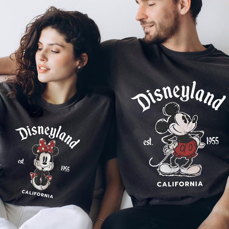 May include: Dark grey t-shirts featuring the Disneyland logo and Mickey and Minnie Mouse designs. The shirts display the word "Disneyland" in a script font, with "est. 1955" and "CALIFORNIA" beneath the character illustrations.