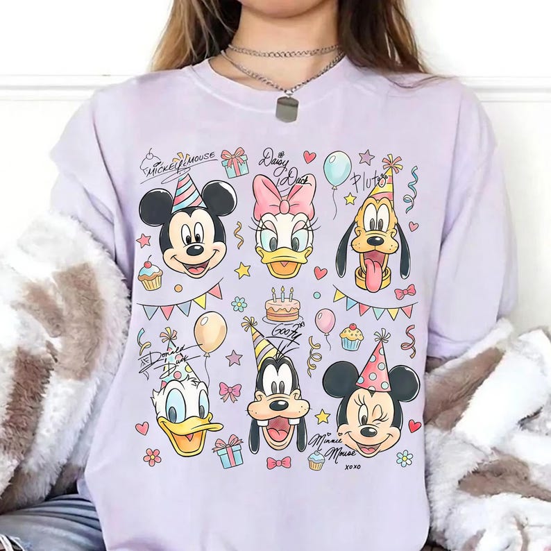 May include: A light purple sweatshirt featuring cartoon character faces, including Mickey Mouse, Minnie Mouse, Donald Duck, Daisy Duck, Goofy, and Pluto, all wearing party hats. The design includes balloons, cupcakes, and the text "Mickey Mouse", "Daisy Duck", "Goofy", and "Minnie Mouse".