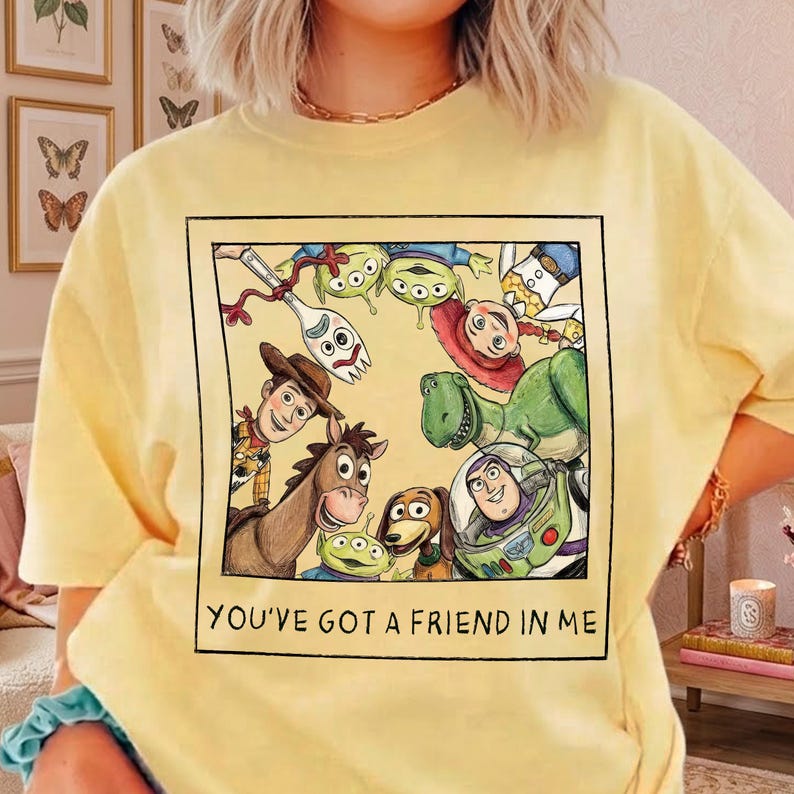May include: Yellow t-shirt featuring a framed graphic of Toy Story characters, including Woody, Buzz Lightyear, and the aliens. The text "YOU'VE GOT A FRIEND IN ME" is printed below the graphic. The shirt is a casual, comfortable style.