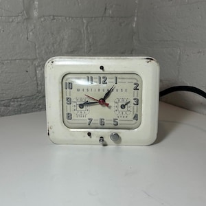May include: Vintage Westinghouse electric clock in a cream metal case. The clock face has black numerals and hands, with the word "Westinghouse" printed in the centre. Features a start and stop dial.