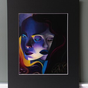 May include: A framed artwork featuring a stylized portrait of a woman's face. The painting uses a palette of blues, purples, and yellows to create a dramatic effect. The woman's lips are a deep purple, and her hair is a mix of dark and golden tones.