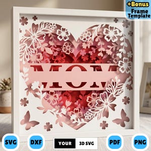 Puede incluir: Una pieza de arte en papel SVG 3D enmarcada en blanco con un diseño en forma de corazón. El corazón está lleno de capas de recortes de papel rojo y rosa de flores, mariposas y la palabra "MOM". El marco incluye el texto "+Bonus Frame Template".