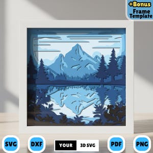Può includere: Un'opera d'arte in carta a strati raffigurante un paesaggio montano con un lago e alberi, nei toni del blu. Il testo "+Bonus Frame Template" è visibile. L'opera è incorniciata in una cornice quadrata bianca. In basso sono presenti icone SVG, DXF, YOUR 3D SVG, PDF e PNG.