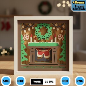 Pode incluir: Uma peça de arte em papel em camadas em uma moldura branca, apresentando uma cena de Natal. O design inclui uma coroa verde, velas, uma lareira com as calças do Papai Noel e árvores de Natal. A imagem também inclui o texto "+Bonus Frame Template".