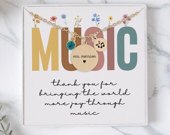 May include: A gold-colored necklace with a pendant that says "mrs. morrison" and a heart. The necklace is on a white card with the word "MUSIC" in colorful letters and the text "thank you for bringing the world more joy through music."