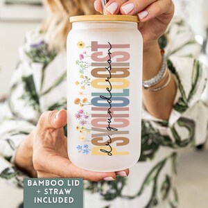May include: A frosted glass can-shaped tumbler with a bamboo lid and straw. The tumbler features the word "PSYCHOLOGIST" in colorful vertical text, with the name "dr. gunderson" in script. Floral accents decorate the side.