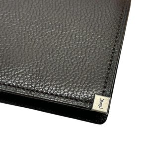 Peut inclure: Portefeuille en cuir noir avec une surface textur&eacute;e. Un petit embl&egrave;me carr&eacute; argent&eacute; avec un logo est visible sur le coin. Le portefeuille semble neuf et inutilis&eacute;.