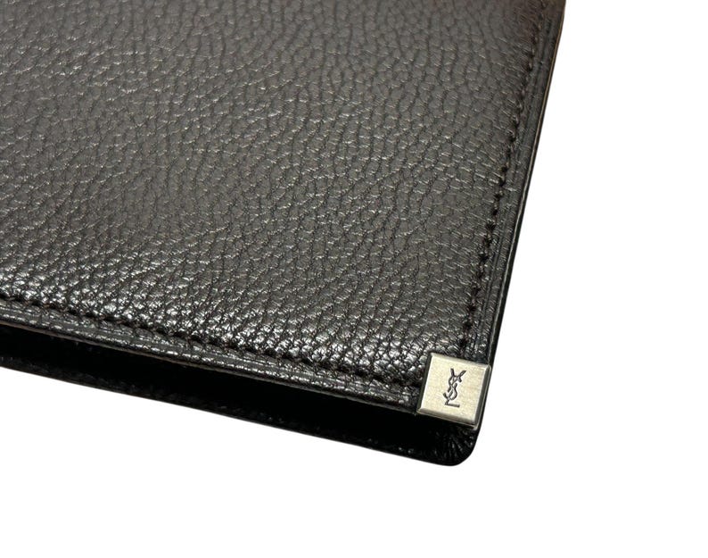 Peut inclure: Portefeuille en cuir noir avec une surface textur&eacute;e. Un petit embl&egrave;me carr&eacute; argent&eacute; avec un logo est visible sur le coin. Le portefeuille semble neuf et inutilis&eacute;.