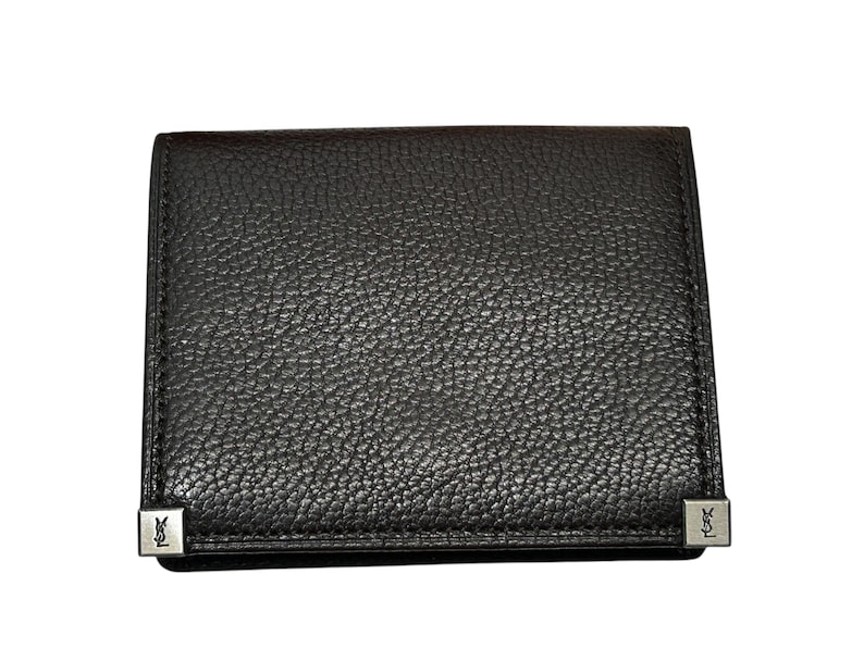 Peut inclure: Un portefeuille en cuir marron fonc&eacute; avec une surface textur&eacute;e. Le portefeuille est de forme rectangulaire et comporte des accents m&eacute;talliques argent&eacute;s sur les coins. Les accents m&eacute;talliques ont un logo. Le portefeuille est ferm&eacute;.