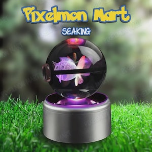May include: A spherical, clear glass ornament with a 3D Seaking design, illuminated with purple and pink light. The ornament sits on a silver base, with the text "Pixelmon Mart" and "Seaking" above it.