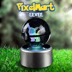 Peut inclure: Une boule de cristal noire et transparente avec une figurine Eevee lumineuse à l'intérieur, posée sur une base argentée. Le texte "PixelMart" et "EEVEE" est visible. L'Eevee est illuminé de lumières bleues, vertes et violettes.