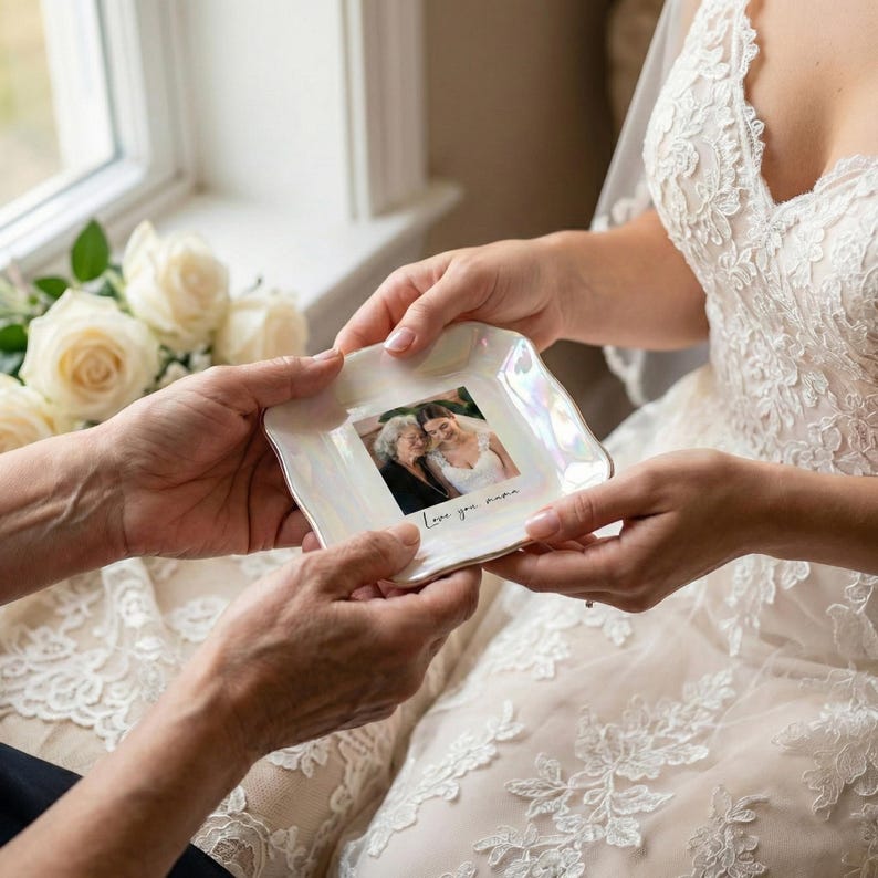 May include: A square, iridescent white trinket dish with a photograph and the handwritten text "Love you, mama." The dish is held by two people, with a bride in a lace wedding dress in the background.