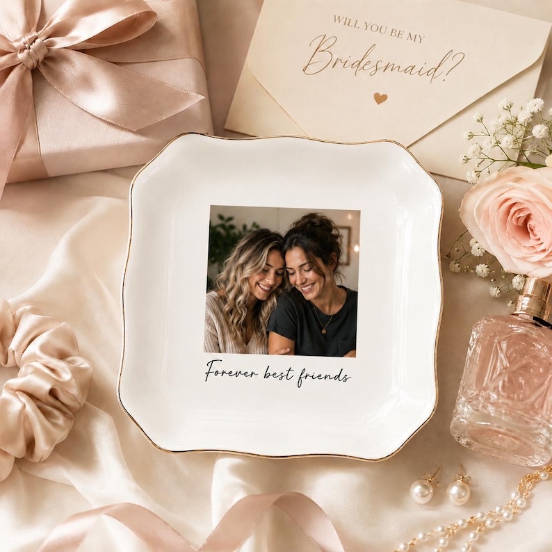 May include: A white ceramic trinket dish with a gold rim, featuring a photo of two smiling women and the text "Forever best friends." The dish is surrounded by a gift box, flowers, and jewelry.