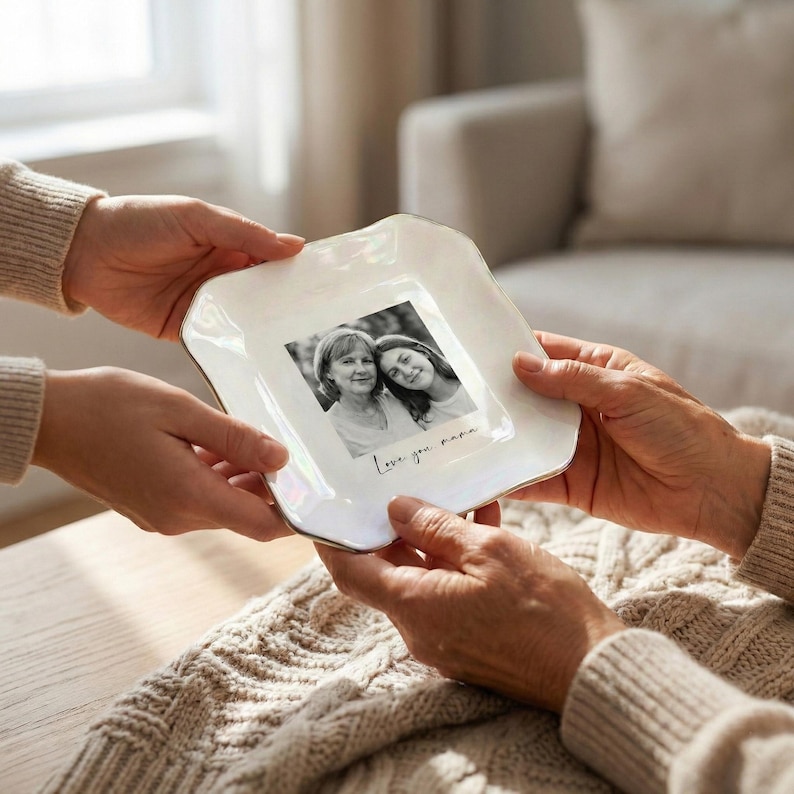 May include: A white, square-shaped ceramic dish with a gold trim, holding a black and white photograph of two women. The photo is inscribed with the words "Love you, mama."