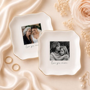 May include: Two white ceramic trinket dishes with gold trim, each featuring a photograph. One shows a bride with an older woman, the other a mother and child. The text "Love you, mama" is written on the dishes.