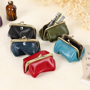 May include: A collection of colorful leather coin purses with metal clasps. The purses are in various colors, including black, blue, red, and green. Some purses have a letter on the front. One purse is open, revealing folded paper money.