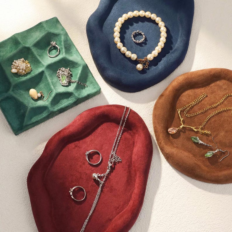 May include: An assortment of jewelry displayed on velvet trays. The trays are in various colors, including green, blue, brown, and red. Jewelry includes rings, necklaces, earrings, and a pearl bracelet.