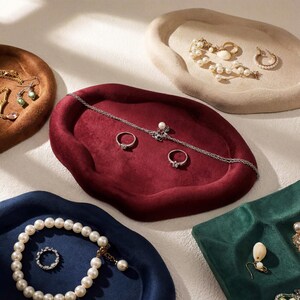 May include: An assortment of jewelry displayed on velvet trays in various colors. The trays are in shades of brown, red, blue, beige, and green. Jewelry includes necklaces, rings, earrings, and bracelets with pearls and gemstones.