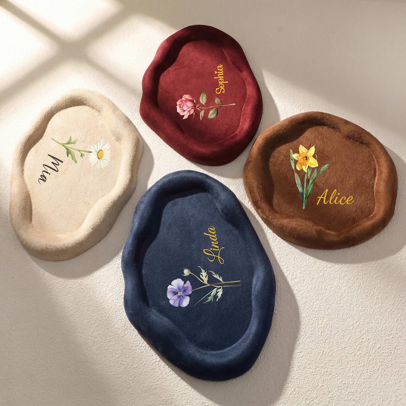 May include: Four decorative, irregularly shaped trays in beige, burgundy, brown, and navy blue. Each tray features a floral design and a name in gold script: Mia, Sophia, Alice, and Linda. The trays are made of a soft, plush material.