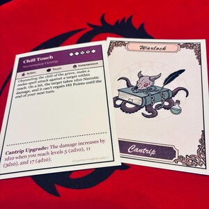 May include: Two fantasy-themed game cards on a red surface. One card features text about "Chill Touch" and "Necromancy Cantrip." The other card has a "Warlock" illustration with a skull, tentacles, and a potion bottle. The cards are for a tabletop game.