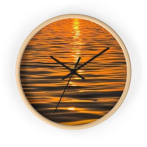 May include: Round wall clock with a natural wood frame. The clock face features a photograph of golden water with black clock hands. The clock hands are pointing at 10:09. The clock has a minimalist design.