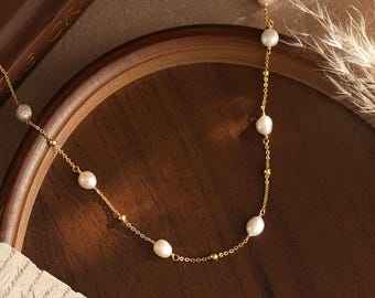 May include: A delicate gold chain necklace featuring evenly spaced white freshwater pearls and small gold beads. The necklace is constructed with a fine link chain that connects each pearl and bead, creating a simple and elegant jewelry piece.