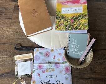 May include: An assortment of stationery items, including a brown leather-bound journal, a floral-covered planner, and a notebook with a pen. A floral pouch with the text "GOD IS Within Her SHE WILL NOT FALL Psalm 46:5" is also present.