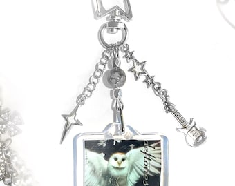 May include: Silver-toned keychain with a star-shaped top, chains, and charms. Charms include stars, a guitar, and a square pendant with an owl image and the word "deftones".