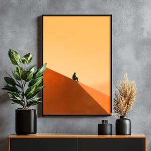 May include: A framed art print featuring a minimalist landscape with a person silhouetted on a sand dune. The artwork has a gradient of orange and yellow hues, with a black frame. Decorative plants and vases are in the foreground.