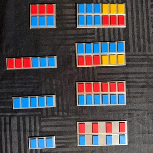 May include: A selection of rectangular badges in red, blue, and yellow. The badges are displayed on a dark surface. Each badge is composed of small, evenly spaced rectangles in different colour combinations.