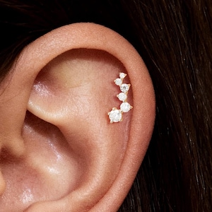 Op de afbeelding: Close-up van een oor versierd met een cluster van kleine, sprankelende diamanten oorbellen. De oorbellen zijn gerangschikt in een delicaat, gebogen ontwerp, wat een vleugje elegantie toevoegt. De huidskleur is licht en de focus ligt op de sieraden.