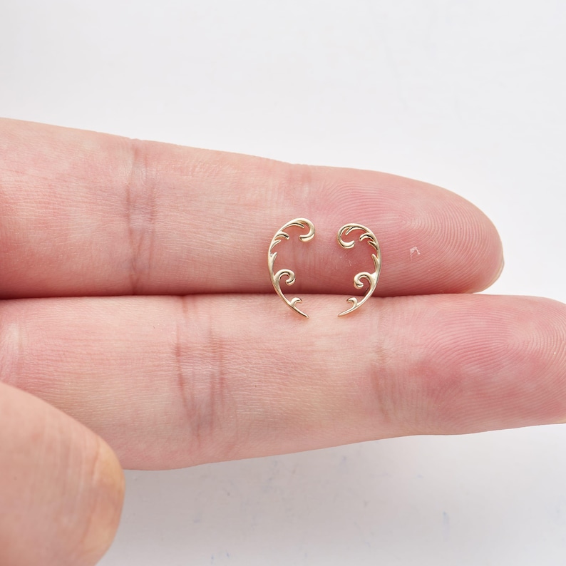 May include: Two delicate, gold-colored earrings with a swirling, floral design. Each earring has a curved shape with intricate details, creating an elegant and artistic look. The earrings are displayed against a neutral background.