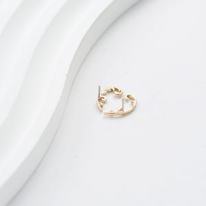 May include: A gold-colored earring with a swirling, openwork design. The earring has a post for insertion and a decorative, curved shape. The earring is set against a white background, highlighting its intricate details and elegant form.