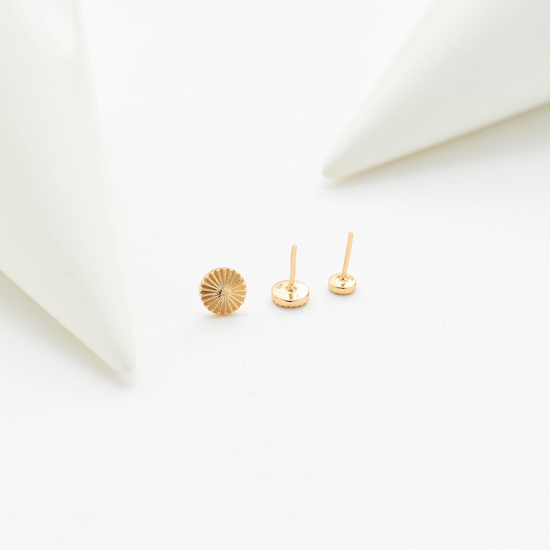 May include: Three gold-colored stud earrings. One earring has a textured, sunburst design, while the other two are simple, round studs with posts. The earrings are displayed on a white surface.