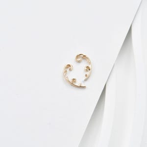 May include: A gold-colored, filigree earring with an open, curved design. The earring features an ornate, swirling pattern with delicate details. The piece is set against a white background, highlighting its intricate craftsmanship. This jewelry item is suitable for various occasions.
