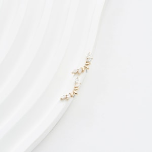 Puede incluir: Un par de trepadores de oreja dorados con un dise&ntilde;o delicado. Cada trepador presenta una serie de piedras preciosas claras con corte marquesa engastadas a lo largo de una barra curva. Los pendientes se muestran sobre una superficie blanca y curva.