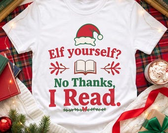 May include: A white short-sleeve t-shirt featuring a red and green graphic of a Santa hat above an open book icon. The text reads: Elf yourself? No Thanks, I Read. The design is centered on the chest with red and green lettering.