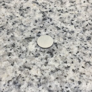 May include: A round, silver-colored metal cover for a hole in a countertop.