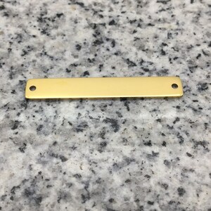 Peut inclure: Une barre en métal de couleur dorée avec deux trous, adaptée à la fabrication de bijoux ou à l'artisanat.