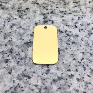 May include: A blank, gold-colored metal tag with a hole at the top for attaching a chain or string.