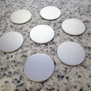 May include: Seven silver-colored metal discs on a gray and black speckled surface.