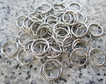 Puede incluir: Un montón grande de llaveros de metal plateado. Los anillos son todos del mismo tamaño y están dispuestos en un patrón aleatorio.