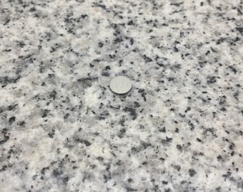 May include: A close-up of a small, round, silver-colored metal disc on a white and gray granite surface.