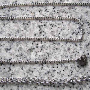 May include: A silver ball chain necklace with a lobster clasp closure. The chain is made of small, round beads.